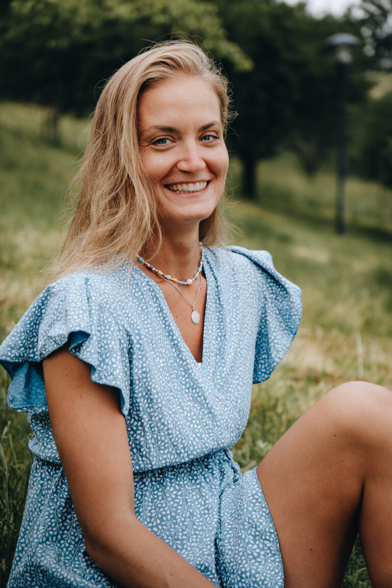 Lifestyle portrét blond ženy v modrých šatech sedící na trávě